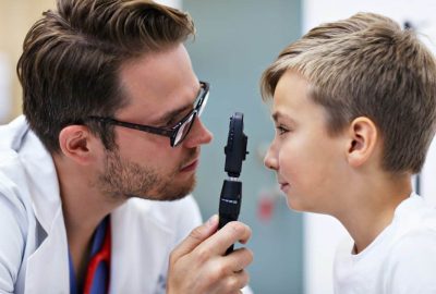 Optometrist examining a young boy’s eyes during a pediatric eye exam.