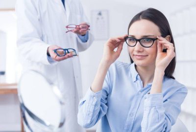 Optician presents eyeglass frames while a client tries on glasses in an optical shop.